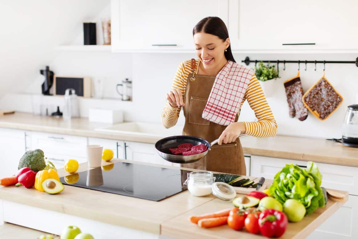 Junge Frau bereitet Fleisch in einer Pfanne zu