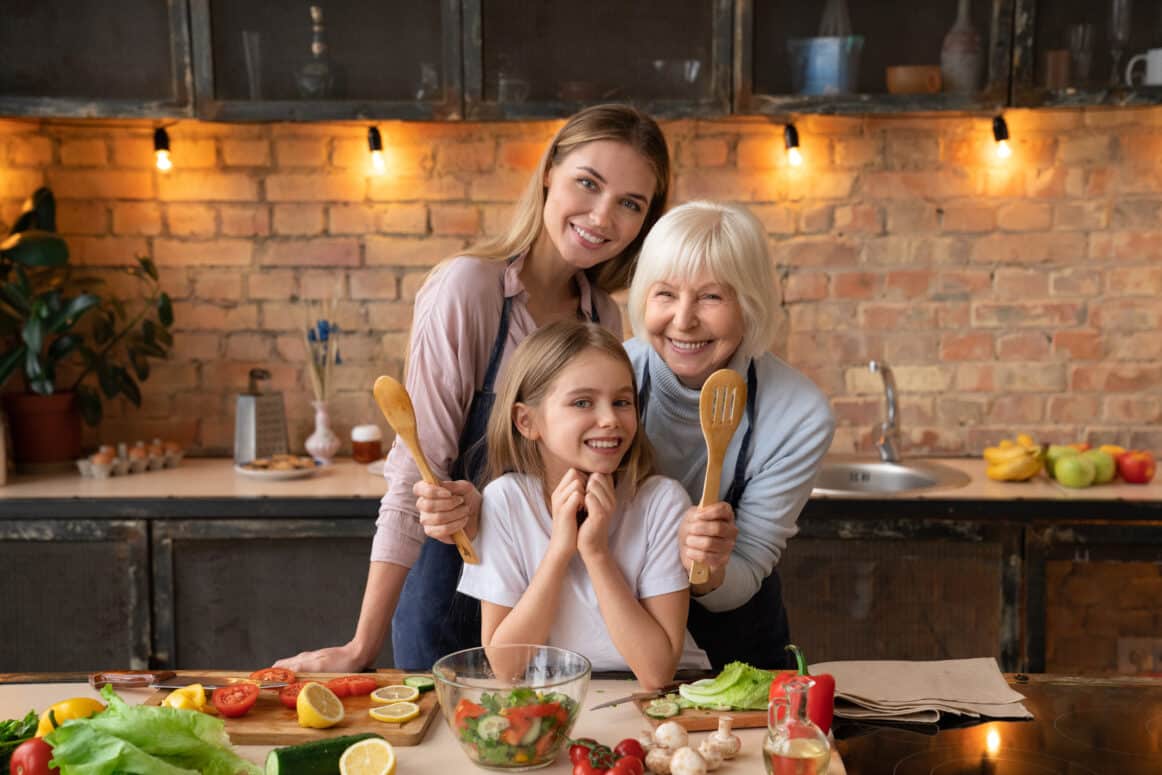 Eine Familie mit Oma, Mutter und Kind in der Küche, die fröhlich in die Kamera schauen