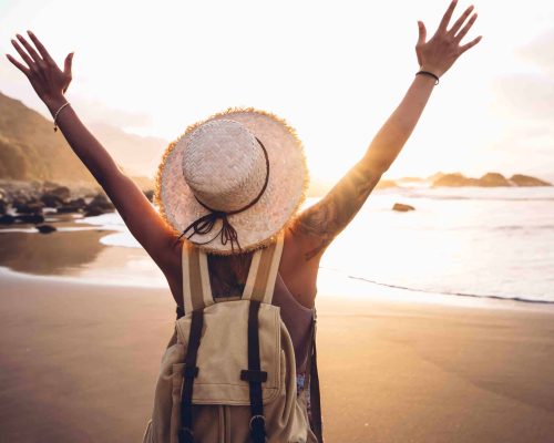 Happy woman with arms up enjoy freedom at the beach at sunset.