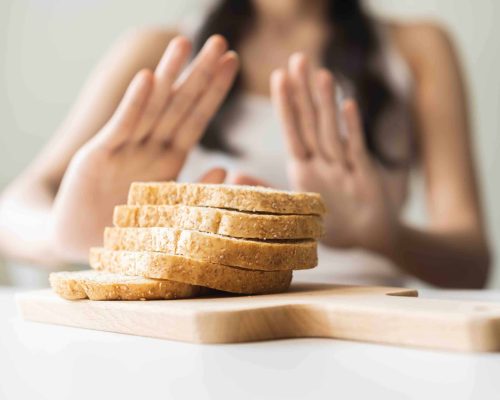 Gluten allergy, asian young woman hand push out, refusing to eat white bread slice on chopping board in food meal at home, girl having a stomach ache. Gluten intolerant and Gluten free diet concept.