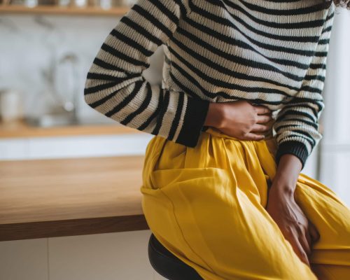 Frau, die auf einem Hocker sitzt und sich vor Schmerzen den Bauch hält